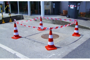 Červenobílé dopravní kužely spojené pruhovanou páskou vyznačující kanál